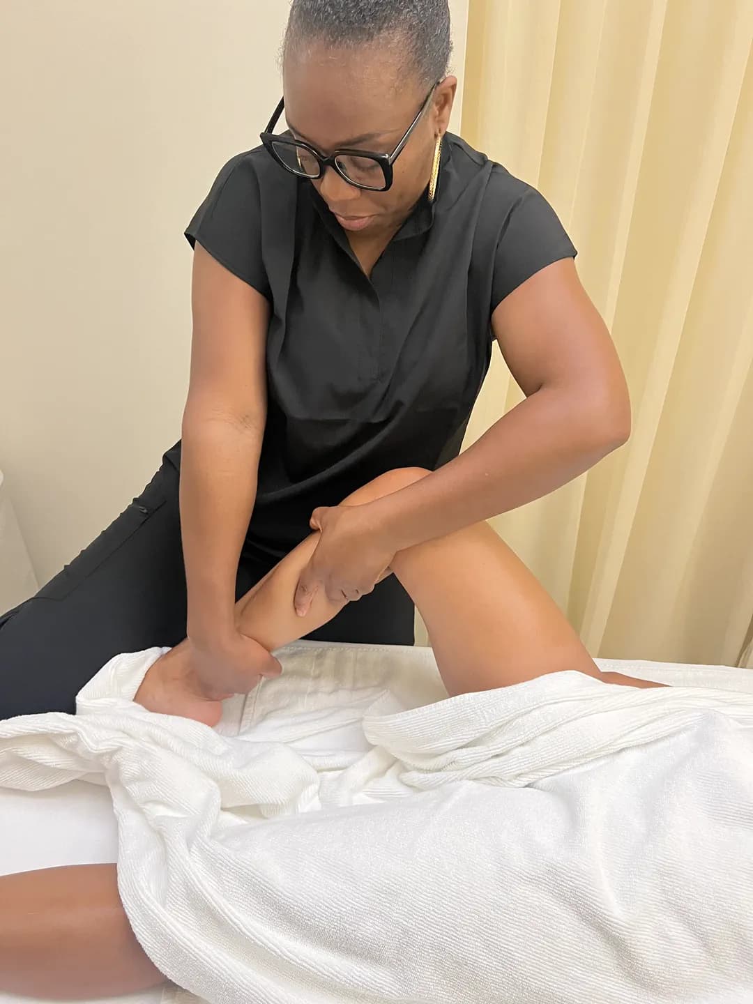 Linda, en tenue noire, exécute une manœuvre de drainage sur la jambe d’une cliente